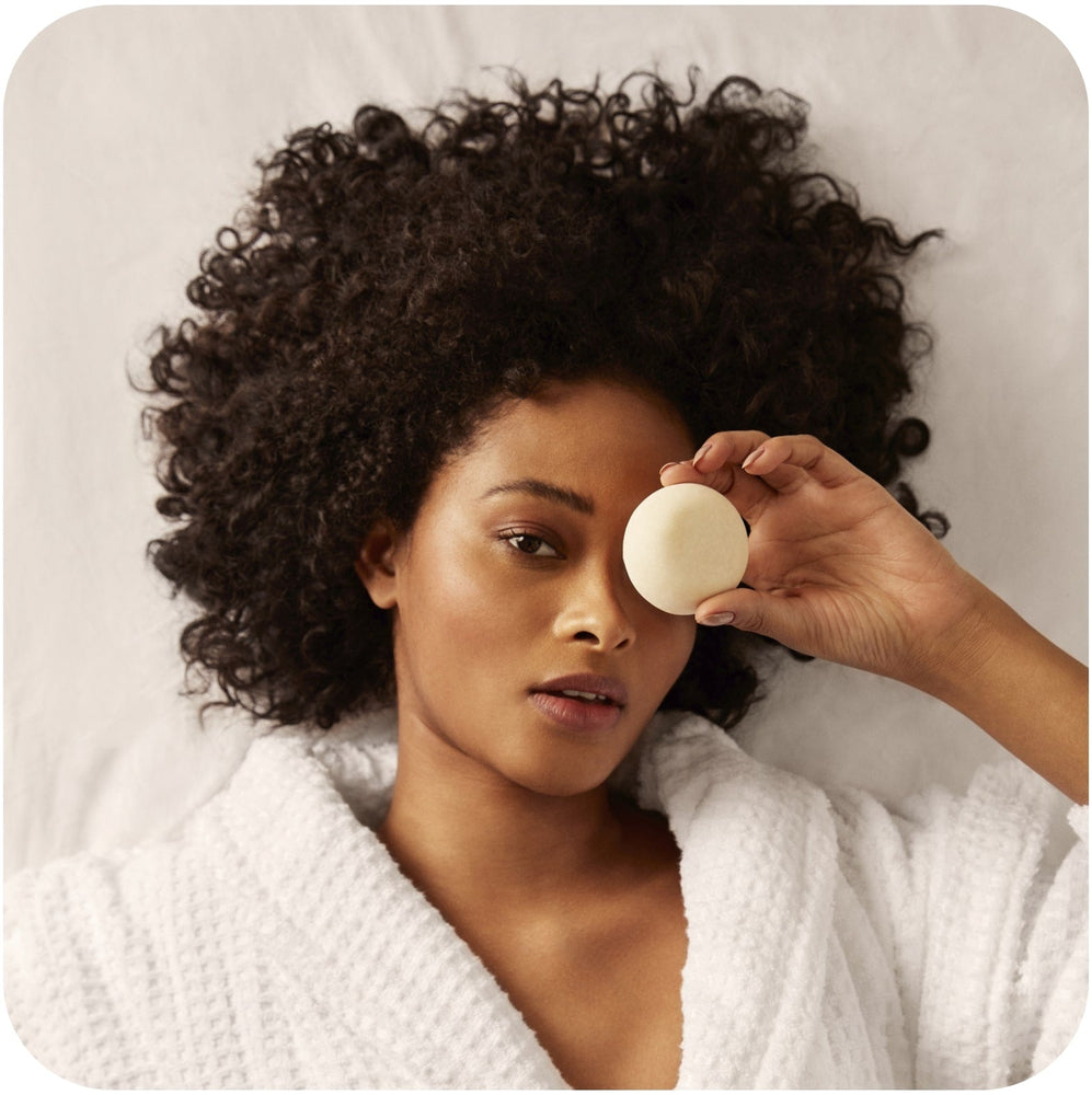 The 2 Best Shampoo Bars for Curly Hair in 2023 Curly-haired woman holding a Bars Over Bottles shampoo bar for curly hair  on her left eye