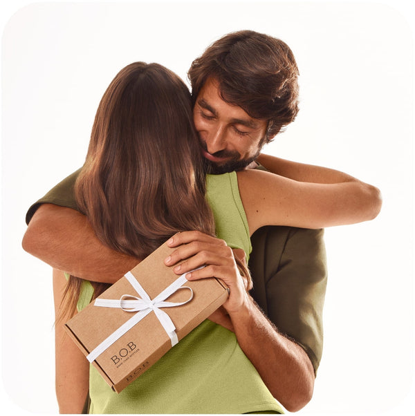 Man hugging his girlfriend while holding a box of Bars Over Bottles curly hair products gift set as a surprise gift