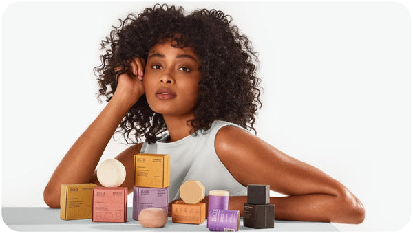 Bars Over Bottles shampoo for curly hair and other beauty products displayed in front of a woman with curly hair