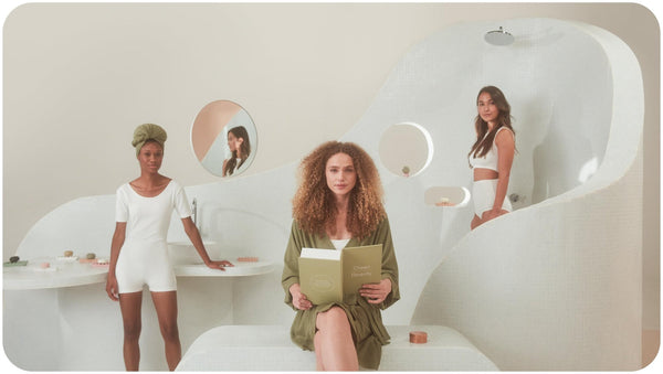 Vegan shampoo and conditioner bars and two women in white behind a woman in green robe holding a book
